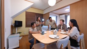 A group of people seated around a wooden table in a room with a television, a small cabinet, and a window with blinds. - A 15-minute taxi ride from Haneda Airport. A perfect standalone house for families and groups to use as a base during their stay in Tokyo. (Ota-ku)