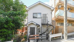 A two-story residential building with a staircase leading to the upper floor, a small balcony, and a door with a window. - A 15-minute taxi ride from Haneda Airport. A perfect standalone house for families and groups to use as a base during their stay in Tokyo. (Ota-ku)