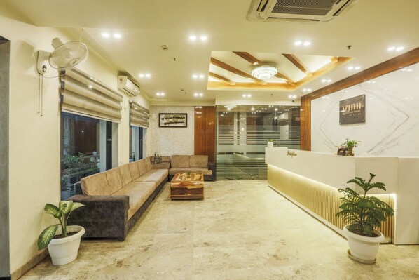 A reception area with a sofa, a wooden coffee table, potted plants, and a reception desk. - VINN Signature Prime by Vesta (Jaipur)