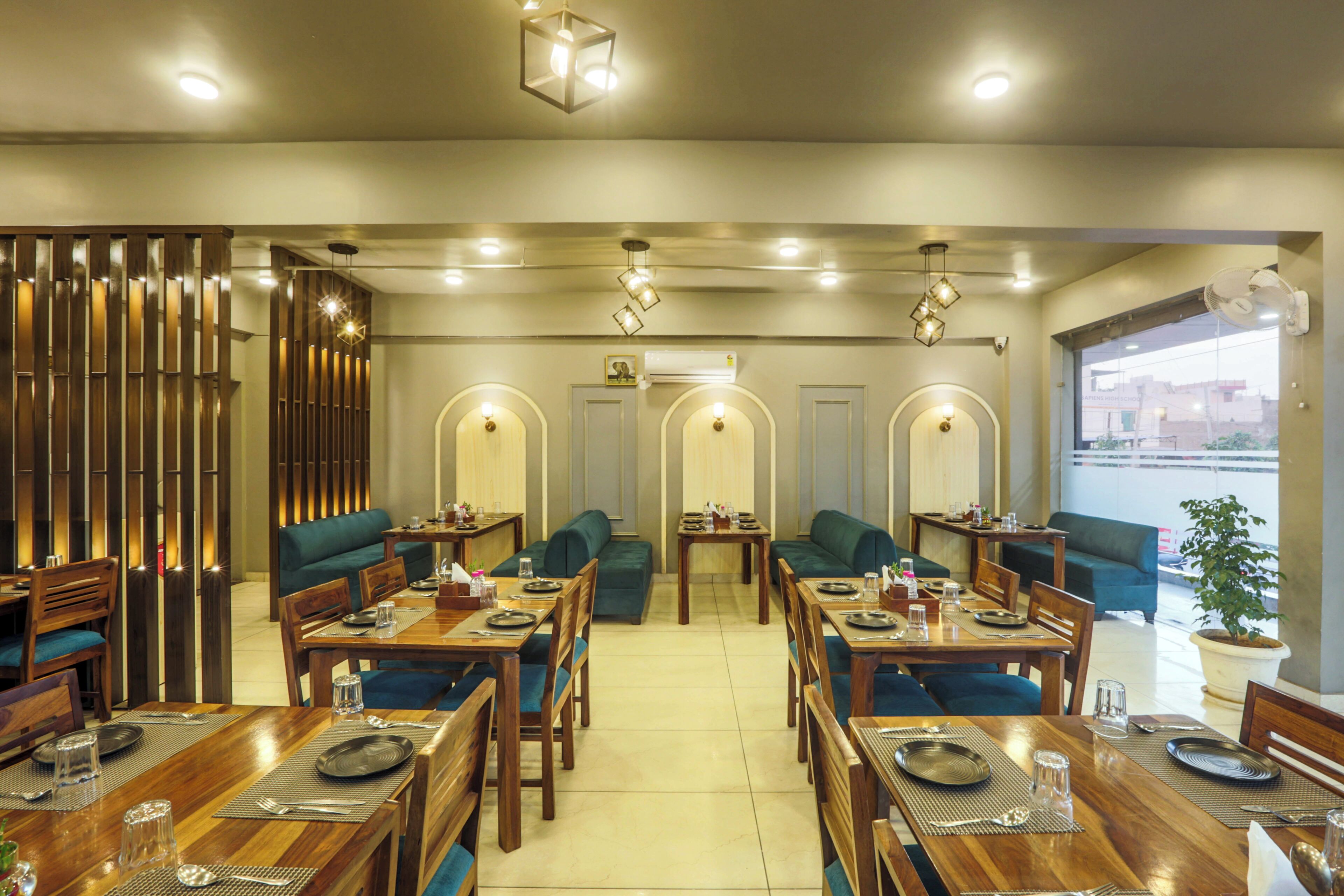 A restaurant with wooden tables and green cushioned seating, a decorative wall, and a view through a large window.