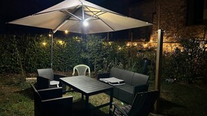 En udendørs terrasse med et bord, stole, en parasol og lyskæder.
