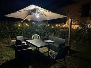 An outdoor patio with a table and chairs, an umbrella, and string lights. - Holiday cottage in the Dordogne – Gite la Grange 24, near Perigueux, Brantome (Saint-Martial-d'Albarède)