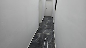 Ein schmaler, gut beleuchteter Gang mit Fliesenboden, weißen Wänden und einer Tür mit der Nummer 101.