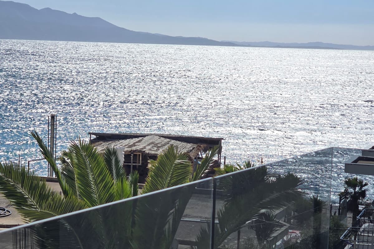 Vista costera con un edificio cerca del agua, palmeras y cielo despejado.