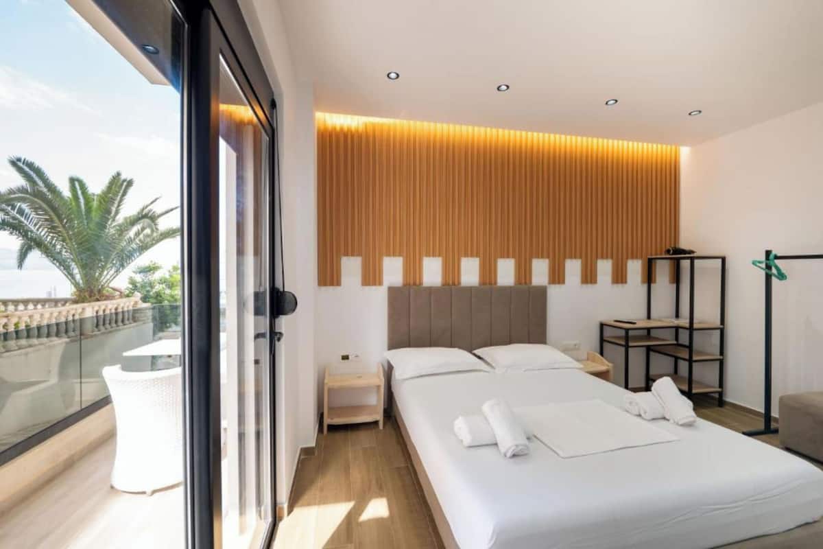 Una habitación de hotel moderna con una cama grande, una mesita de noche y vistas a palmeras.