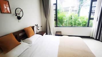 Habitación de hotel con una cama grande, una mesita de noche, una lámpara, un reloj en la pared y una ventana con vistas a zonas verdes.