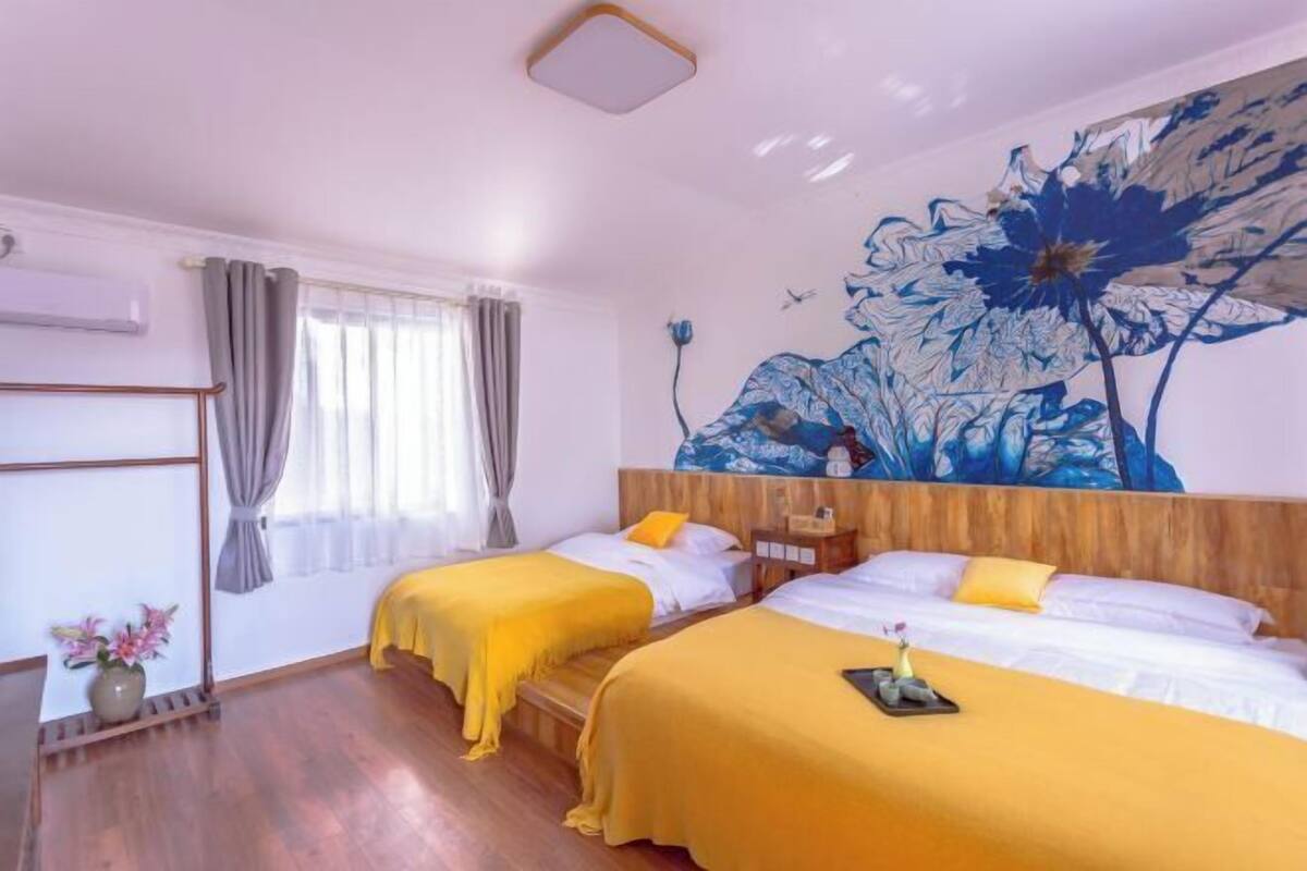 A hotel room with two beds, a large floral mural, a wooden headboard, and a bedside table with a lamp.