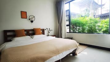 Un dormitorio con una cama grande, una mesita de noche, un reloj y una ventana que ofrece vistas a zonas verdes y arquitectura tradicional.