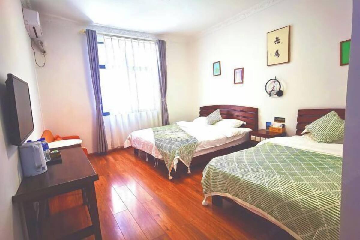 A hotel room with two beds, a desk with a chair, a TV, and a window with curtains.