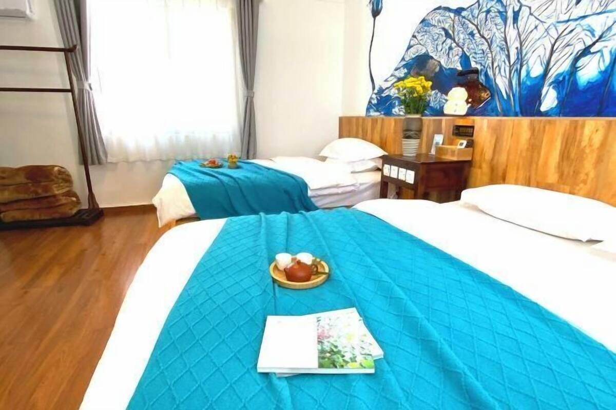 A hotel room with two beds, a wooden headboard, a painting, and a small table with a teapot and cups.