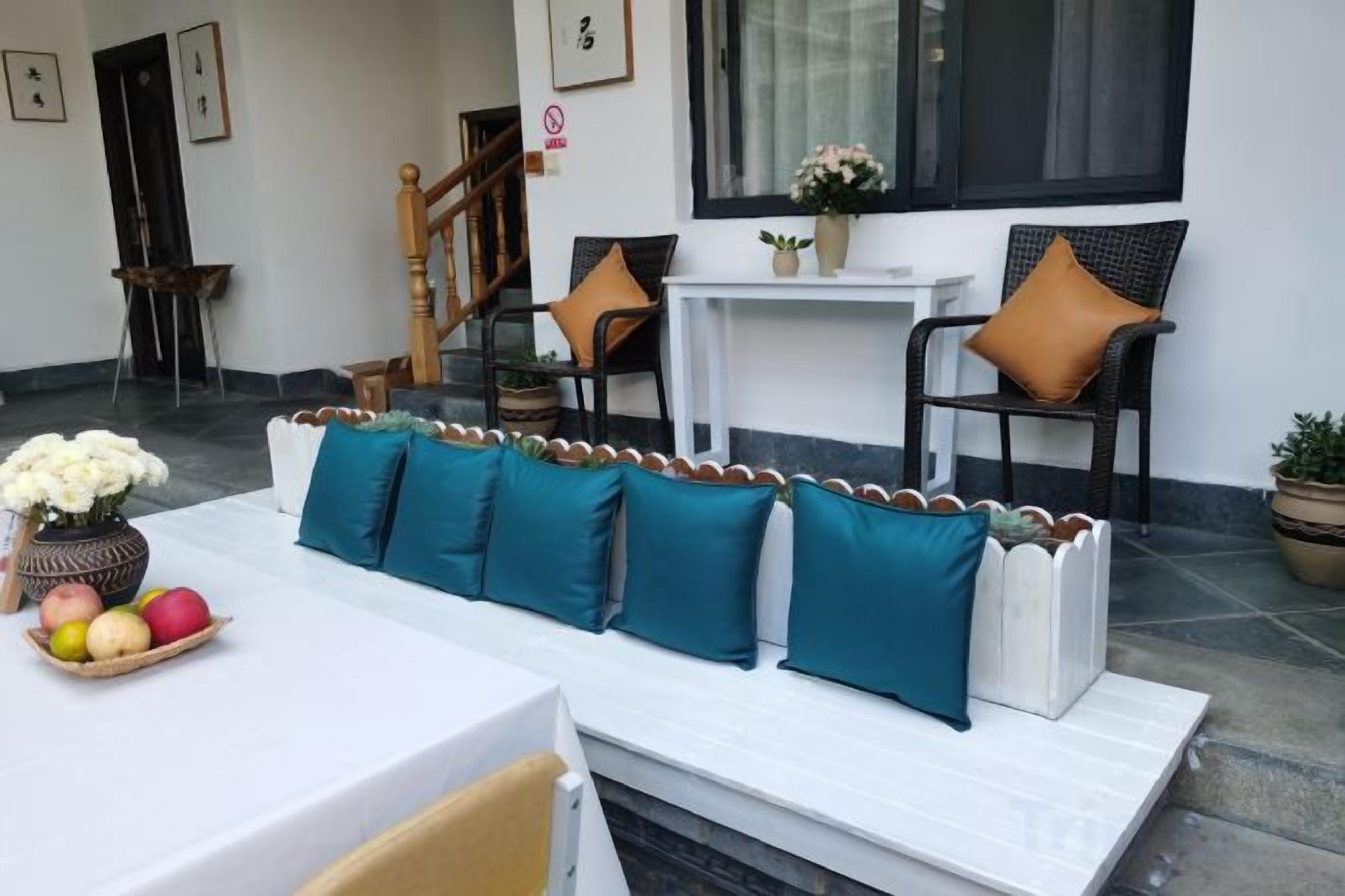 Een zithoek met een witte bank en stoelen, een klein tafeltje met fruit, en een trap op de achtergrond.