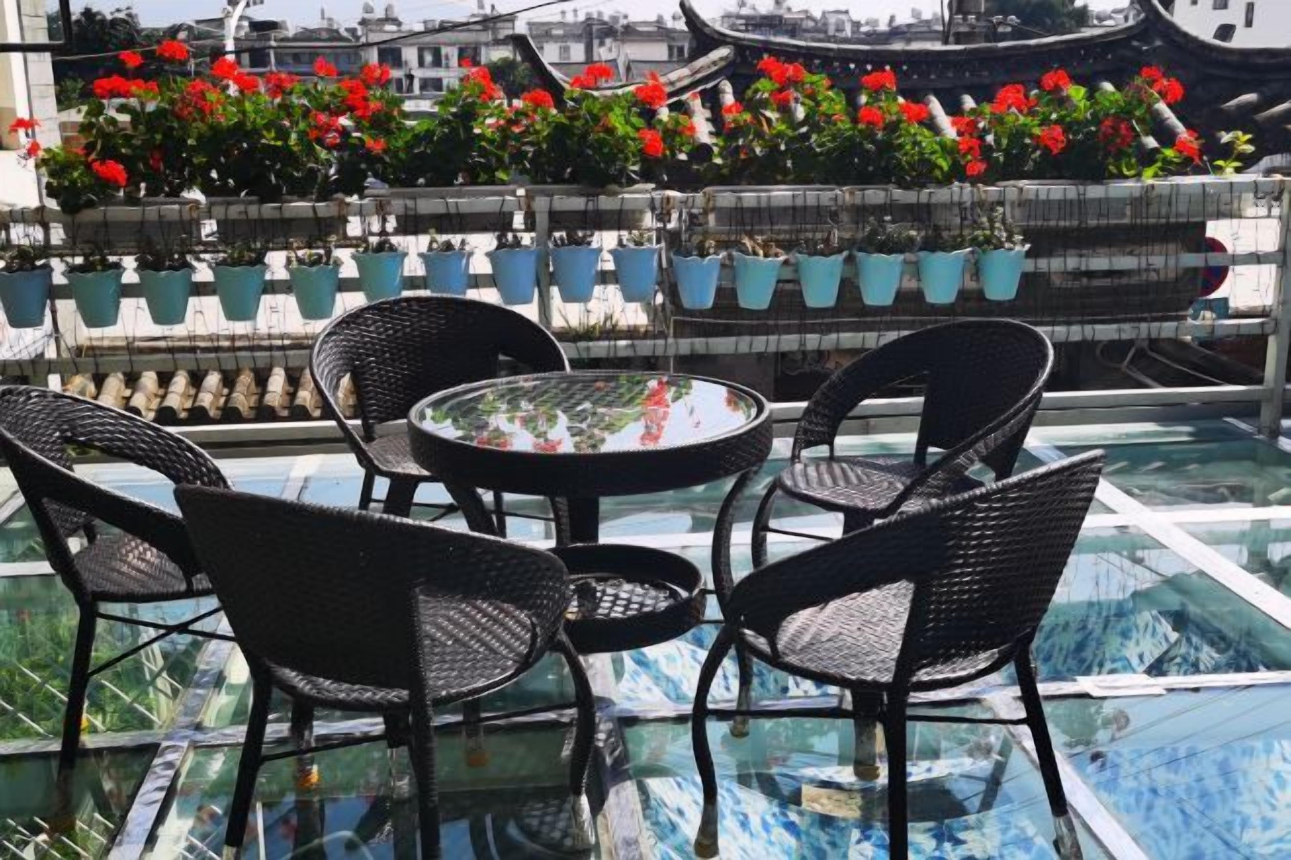 A rooftop terrace with a glass table and chairs, potted plants, and a view of traditional architecture.