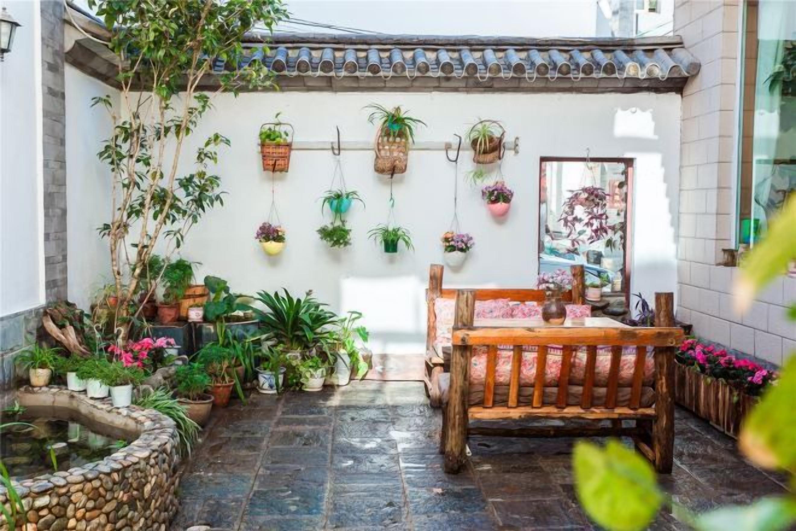 A courtyard with a wooden table and chairs, surrounded by potted plants and hanging planters.
