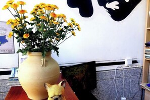 A vase with yellow flowers on a table, a small figurine, and a wall with a map and a black and white design. - 798 Inn (Dali)