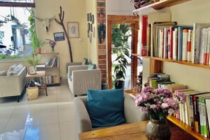 A living room with a sofa, a coffee table, and a bookshelf filled with books. There is a vase with flowers on the coffee table. - 798 Inn (Dali)