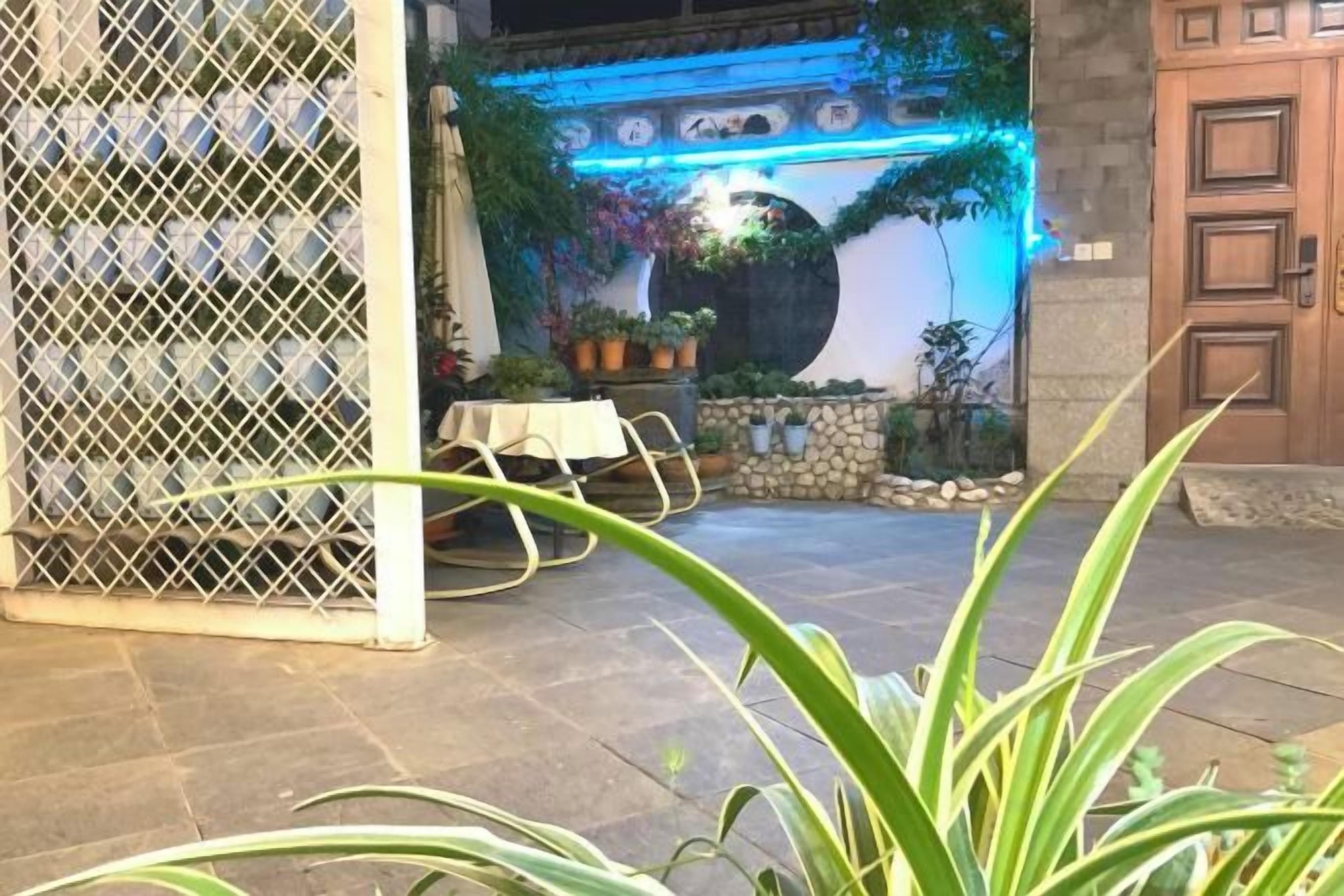 An outdoor patio area with a stone floor, a white table with chairs, and potted plants.
