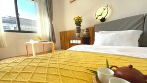 Une chambre d’hôtel avec un lit, une table de chevet ornée d’un vase de fleurs, une horloge et une fenêtre avec des rideaux.