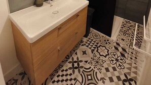 Une salle de bain moderne avec un grand miroir, un meuble-lavabo en bois, un lavabo blanc et une cabine de douche.