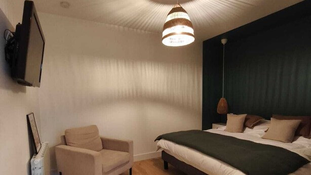 Une chambre à coucher avec un lit, une chaise, un radiateur et un téléviseur fixé au mur.
