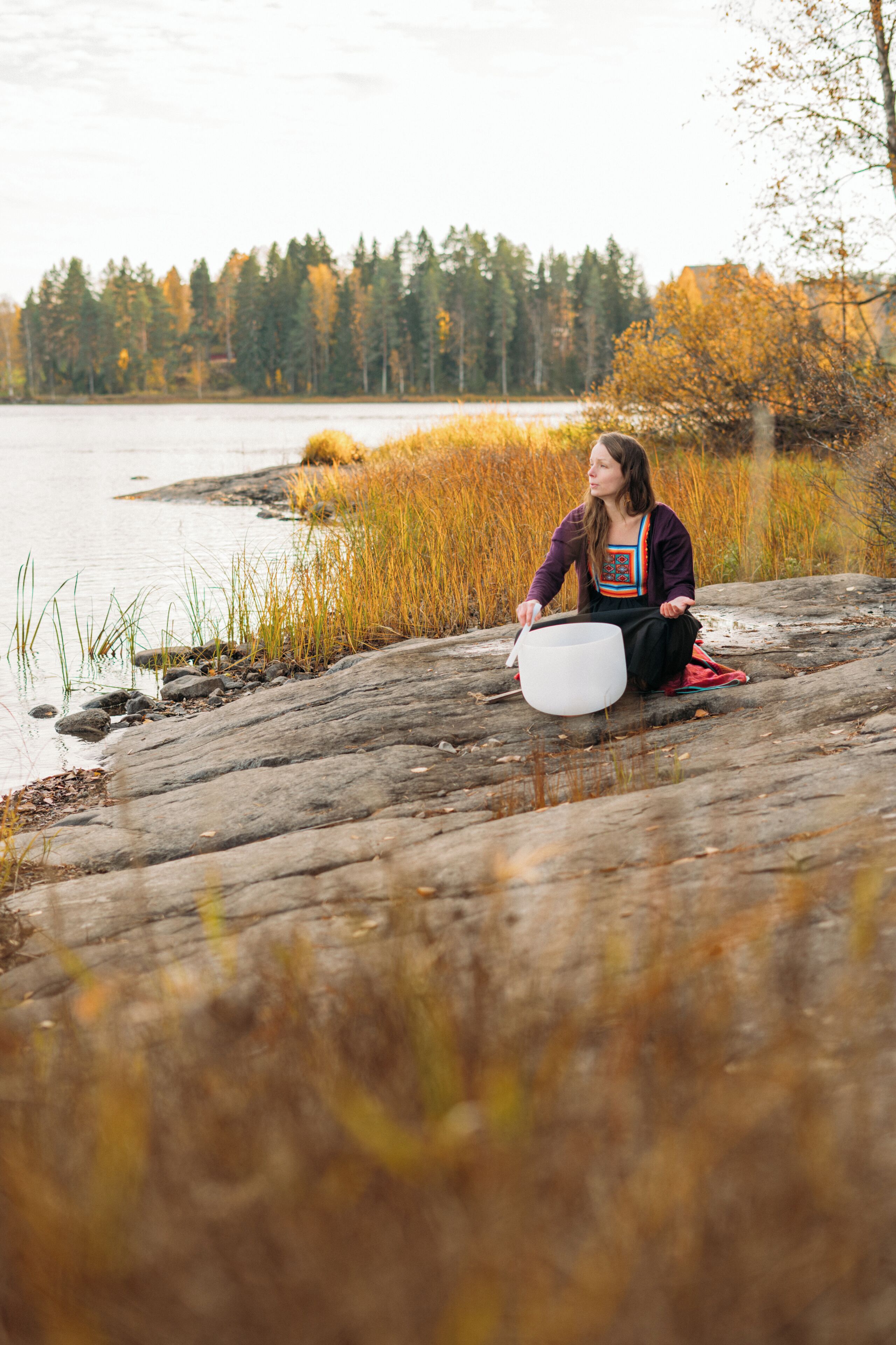 Une personne assise sur une bûche au bord d’un lac, avec des arbres en arrière-plan.