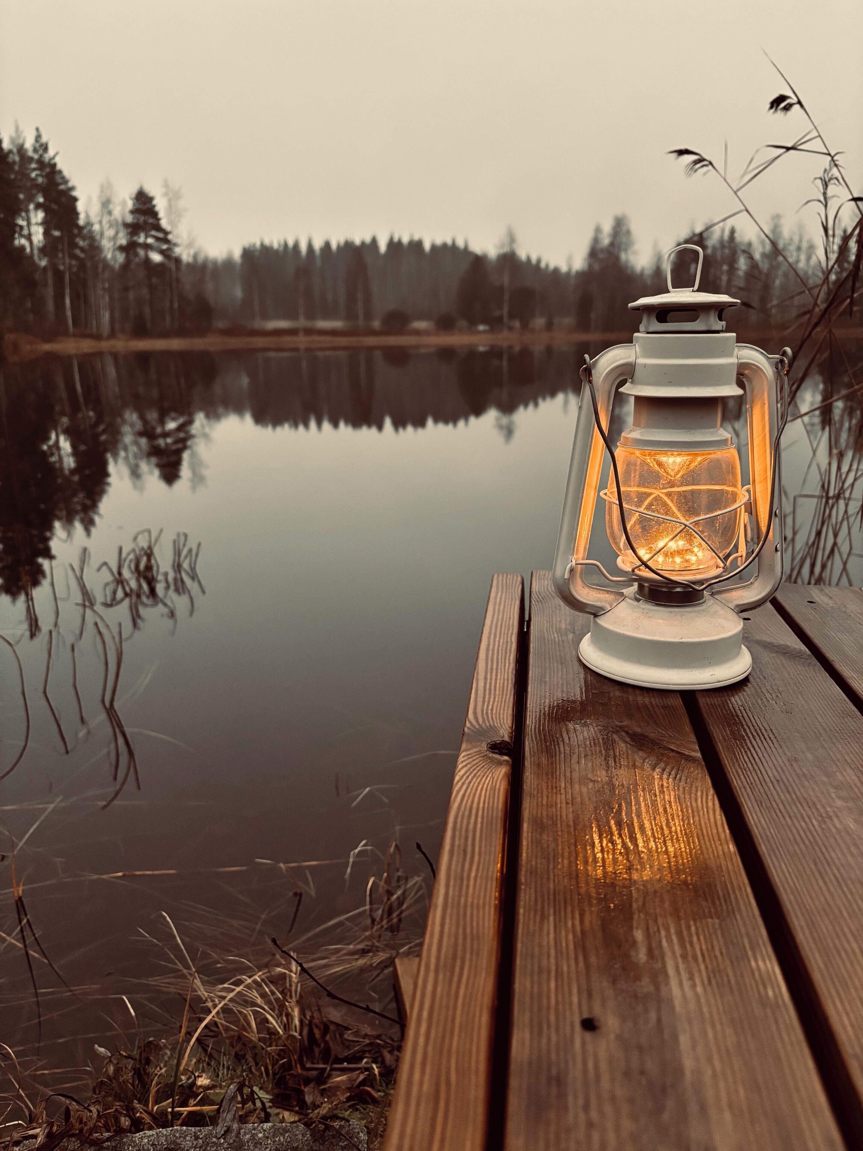 A lantern on a wooden dock by a calm lake with trees in the background.