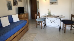 A room with a blue sofa, wooden cabinet, dining table with chairs, and wall-mounted artwork.
