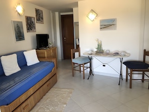 Une piĂšce comprenant un canapĂ© bleu, un meuble en bois, une table Ă manger avec des chaises et des Ćuvres dâart accrochĂ©es au mur.