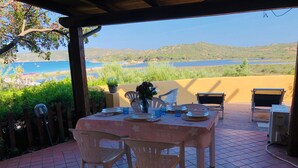An outdoor dining area with a view of the sea, a table set with plates and glasses, and a potted plant.