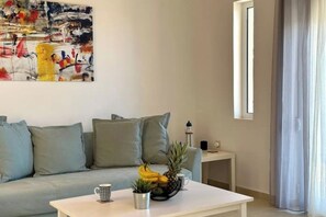 A living room with a sofa, a coffee table with fruits, a small side table, and a painting on the wall. - Aegean View Villa, 2-min Drive to Almyrida Beach with Private Pool and Views (Chania)