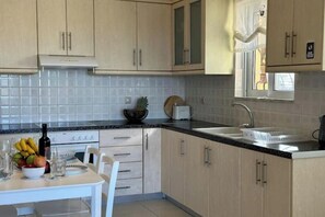 A kitchen with light-colored cabinets, a black countertop, a sink, and a window. - Aegean View Villa, 2-min Drive to Almyrida Beach with Private Pool and Views (Chania)