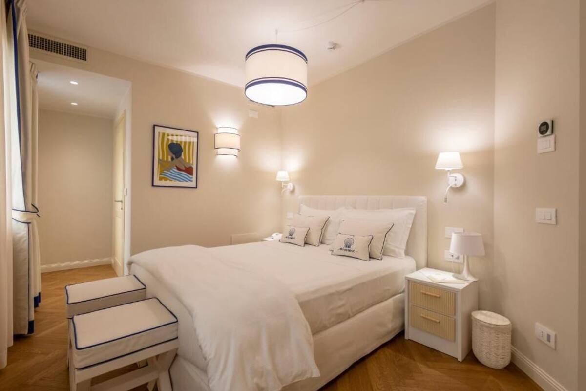 Un dormitorio con una cama grande, mesitas de noche, una lámpara colgante y un cuadro en la pared.