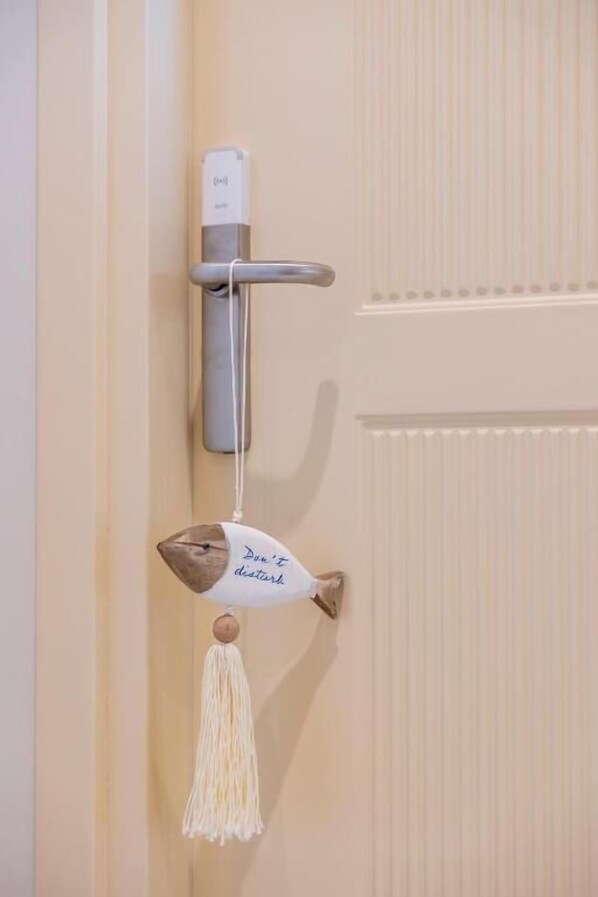 Une porte dotée d’une poignée en métal, un petit appareil blanc placé au-dessus, et un ornement décoratif en forme de poisson, orné de glands pendants.