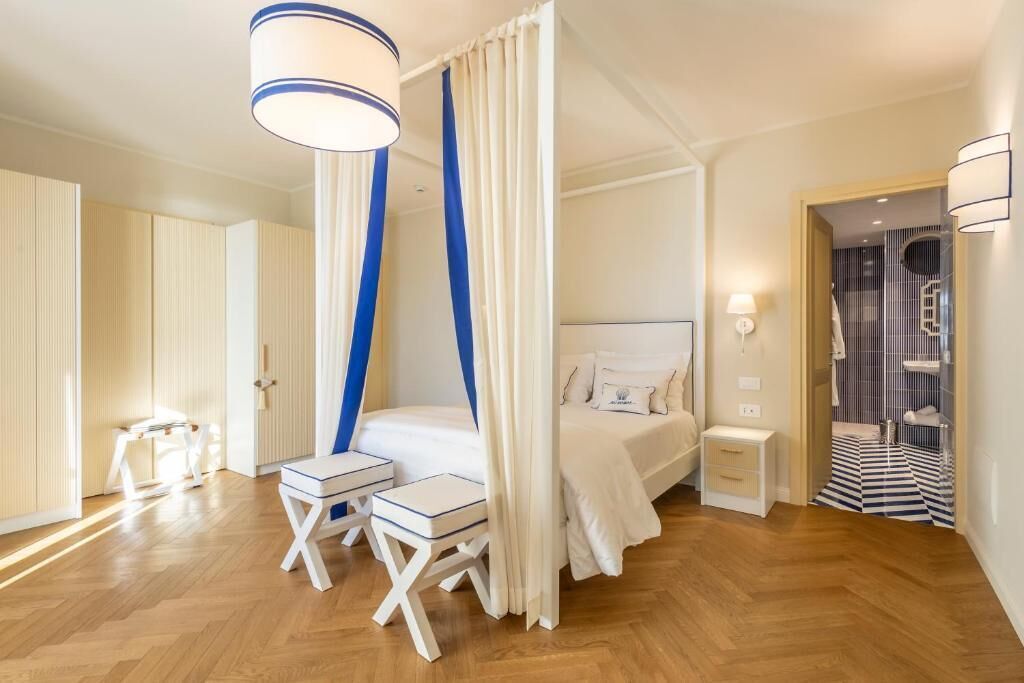A bedroom with a canopy bed, bedside tables, a small seating area, and a bathroom with a striped floor.