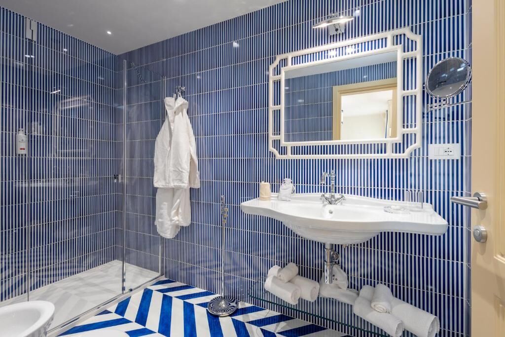 Une salle de bain avec un mur recouvert de carreaux bleus à rayures, un lavabo blanc avec un miroir et un espace douche.