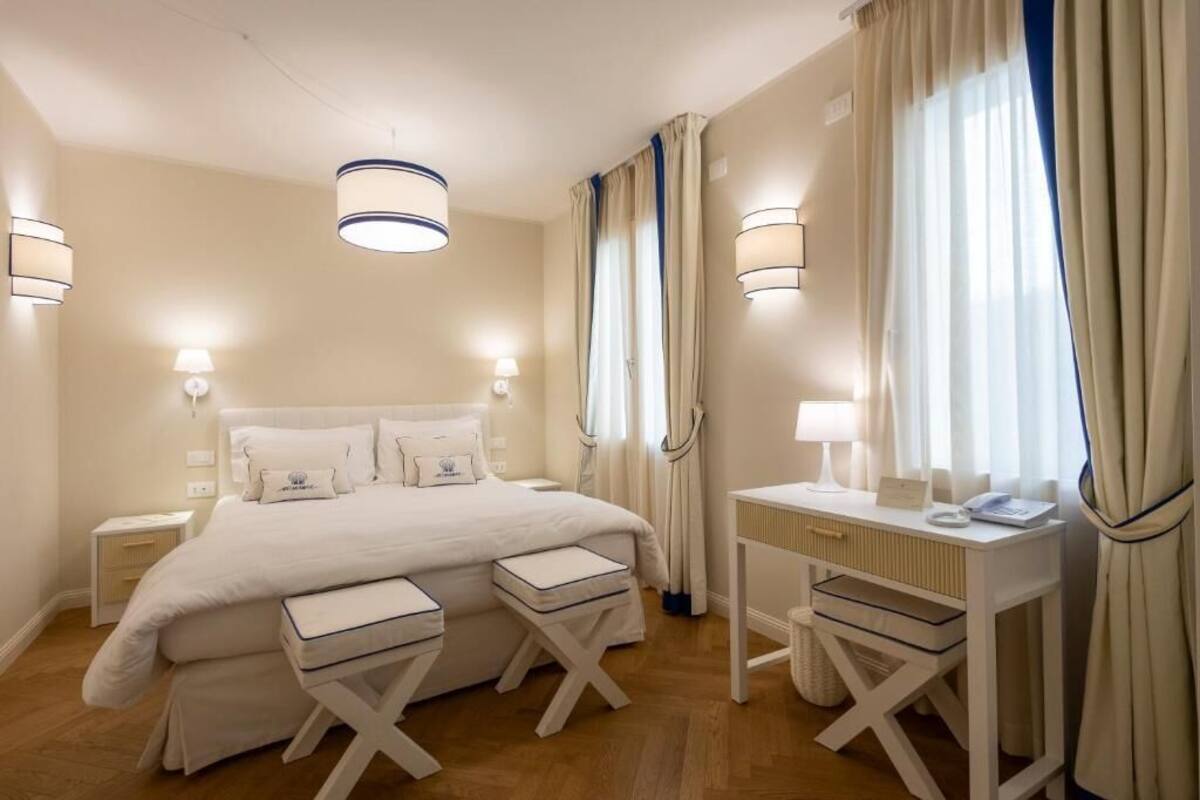 Una habitación de hotel con una cama grande, mesitas de noche, un escritorio y cortinas.