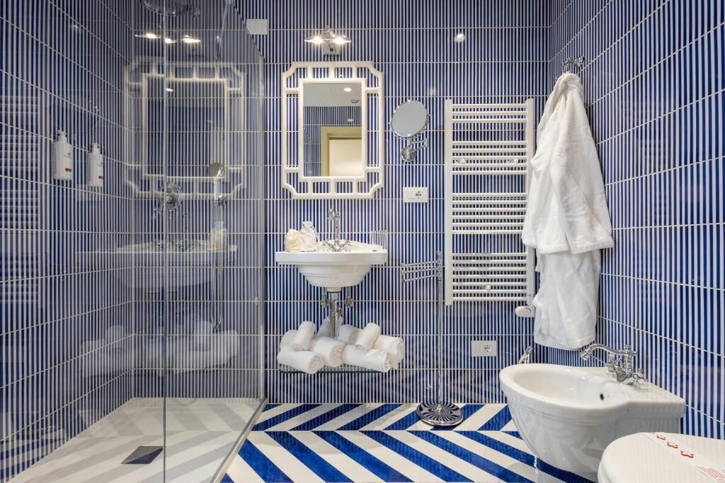 A bathroom with a blue and white striped floor, a white sink, a large mirror, and a bathtub.