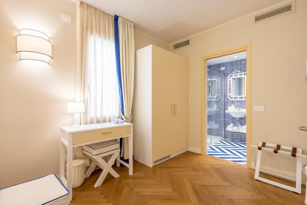 A bedroom with a wooden floor, a white desk with a lamp, a wardrobe, and a bathroom visible through a door.