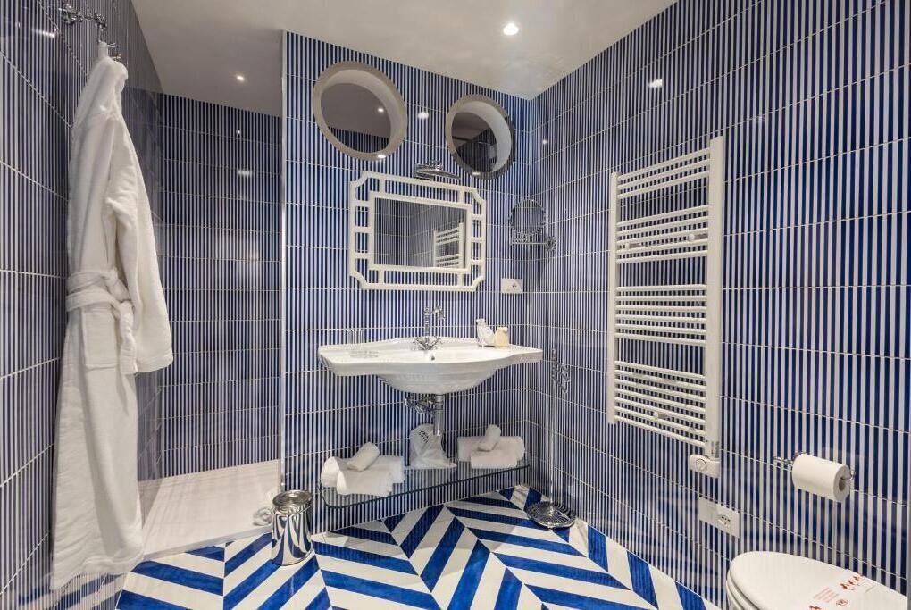 Um banheiro moderno com design de azulejos listrados em azul e branco, pia branca, duas espelhos e área de chuveiro.