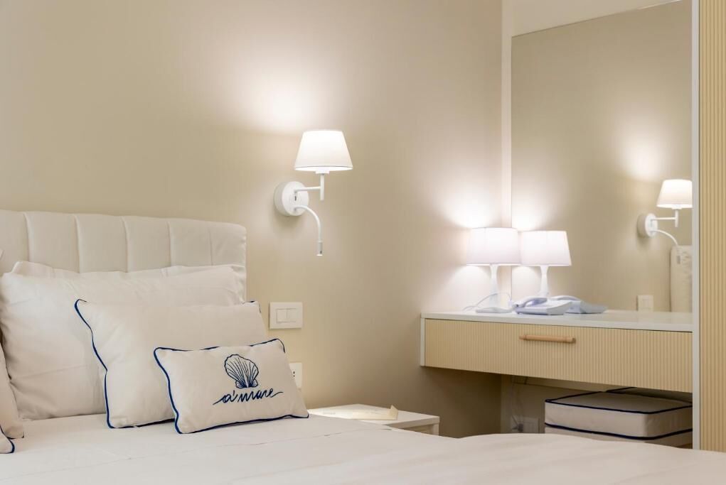 A hotel room with a bed, a bedside table, a mirror, and a nightstand.