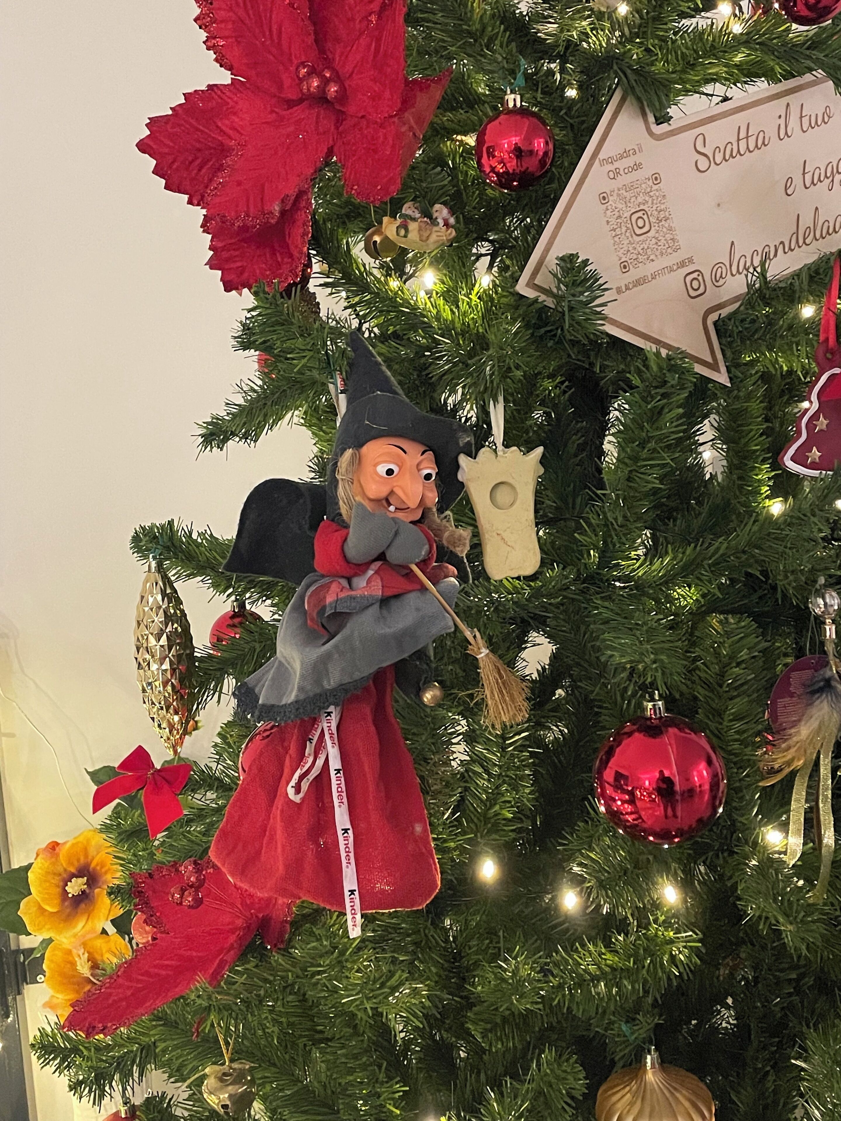 Árvore de Natal com enfeite de homem de gengibre, decorações vermelhas e douradas e um sinal com código QR.