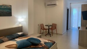 Een hotelkamer met een bed, een klein tafeltje met twee stoelen, een airconditioner en een televisietoestel.