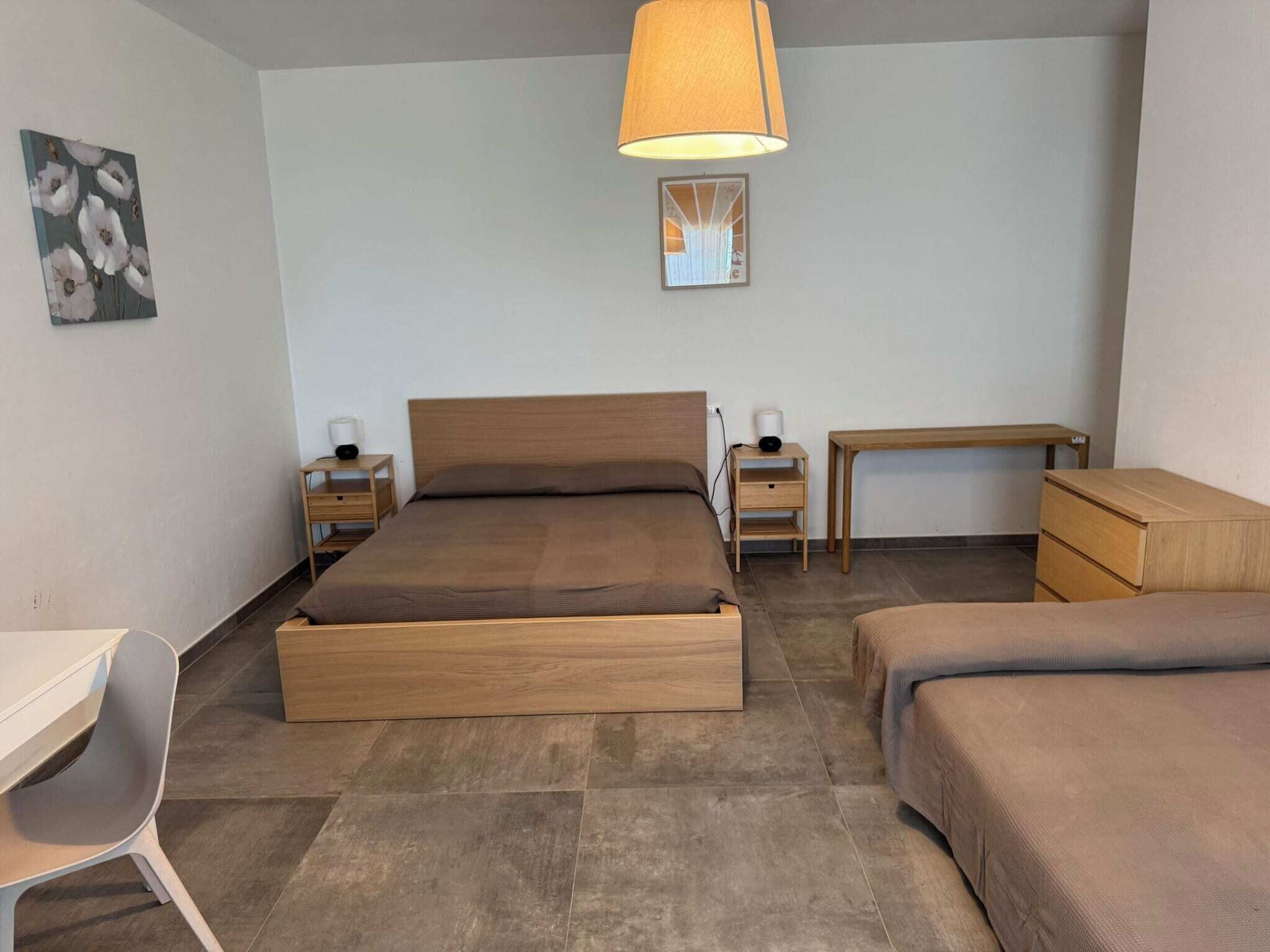 A bedroom with a wooden bed, bedside tables, a desk, and a chair.