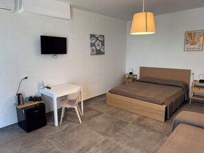 Une chambre à coucher comprenant un lit, un bureau, une chaise, un téléviseur et une table de chevet avec une lampe.
