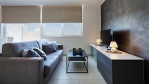 A modern living room with a grey sofa, a coffee table, a TV, and a lamp. - Serene 2BR Penthouse - Sea View Terrace (St. Paul's Bay)