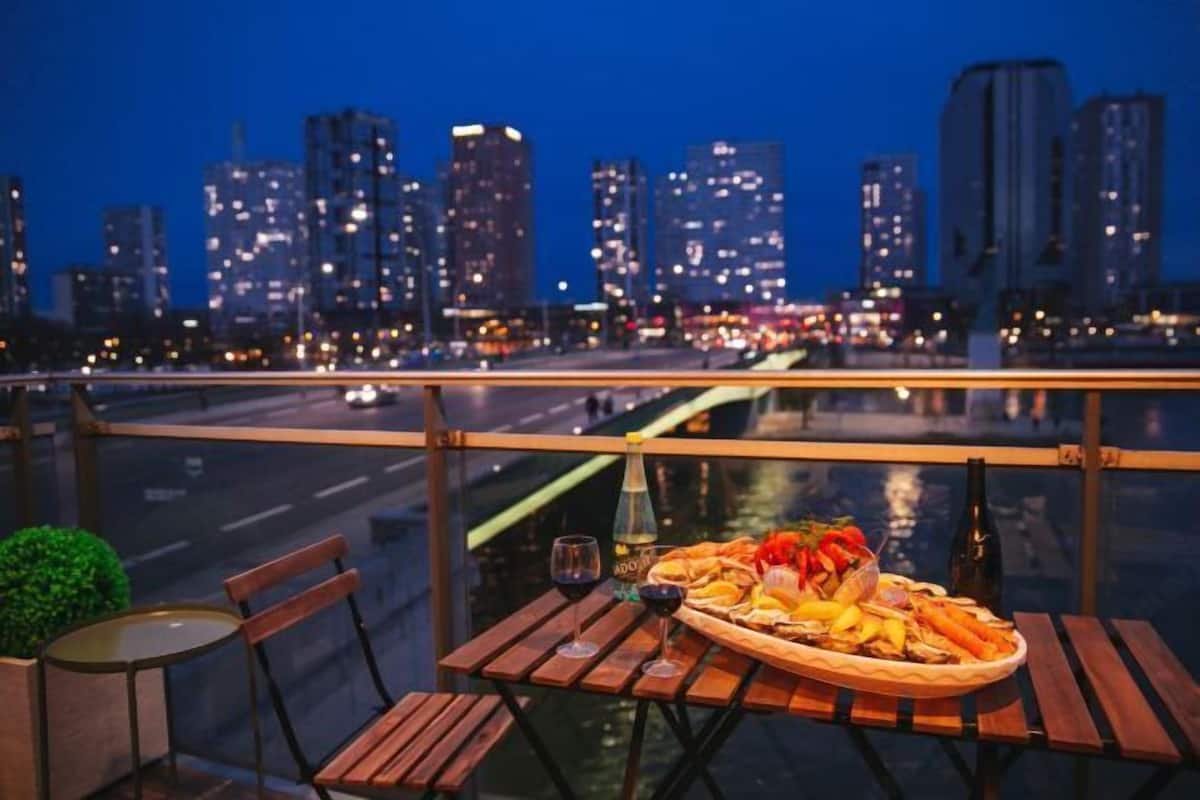 Ein Tisch mit einer Meeresfrüchteplatte, Weingläsern und Flaschen, mit Blick auf eine beleuchtete Stadt bei Nacht.
