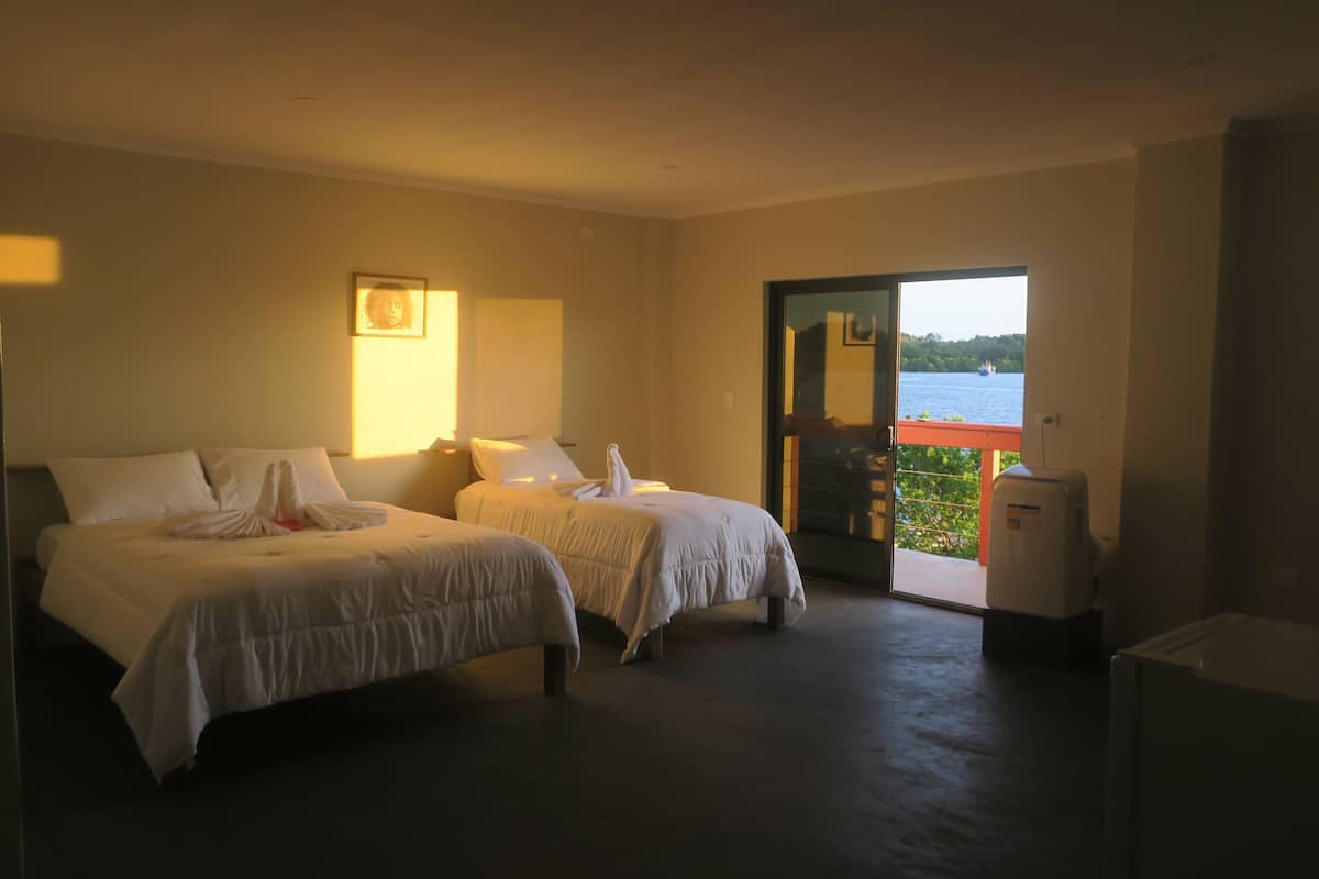 A hotel room with two beds, a small refrigerator, and a view of the sea through a glass door.