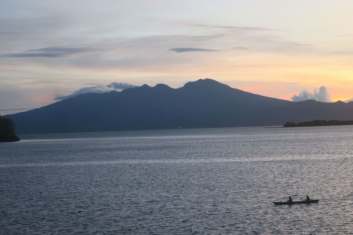 A calm body of water with a mountain in the background and a small boat with two people.