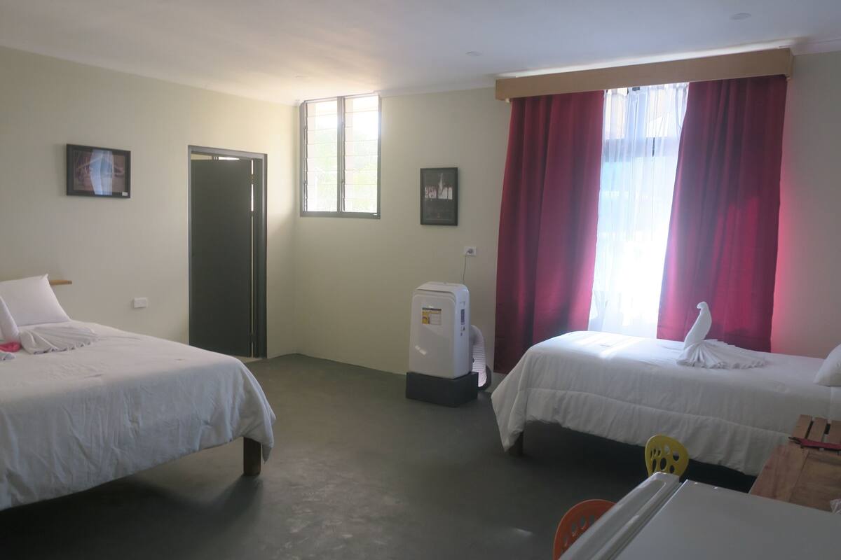 A hotel room with two beds, a heater, a window with curtains, and a door.