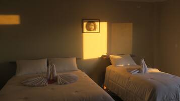 Two beds with towels arranged on them, a framed picture on the wall, and a window casting light into the room.
