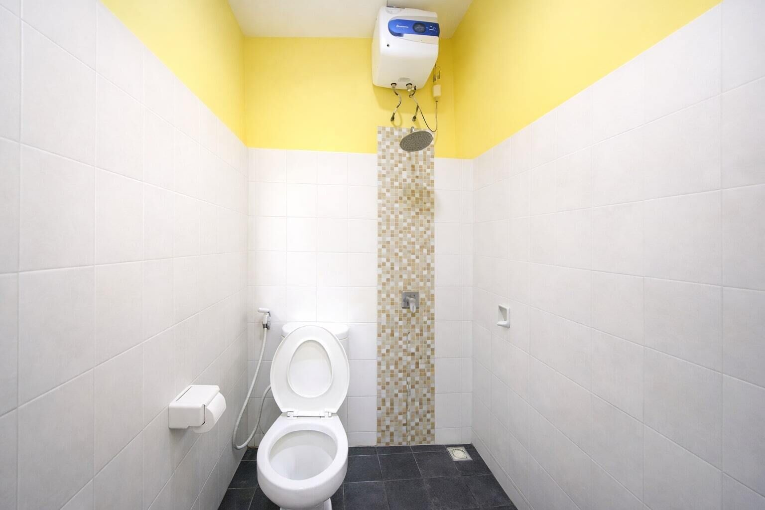 A small, narrow bathroom with white and yellow walls, a toilet, and a shower area.